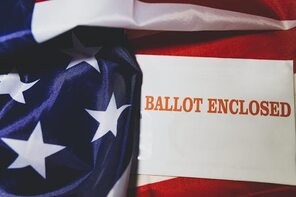 Envelope saying Ballot Enclosed with the US Flag behind it.