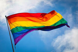 LGBTQ Flag flying against blue sky