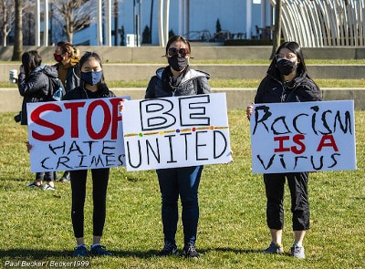 Three women holding signs that say, Stop Hate Crimes, Be United, and Racism is a Virus